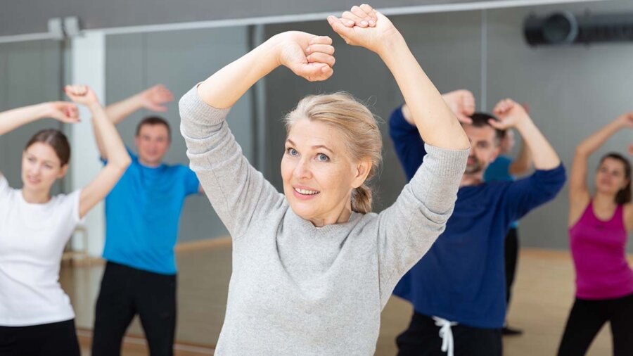 Smiling mature female doing dance workout during group classe in fitness center