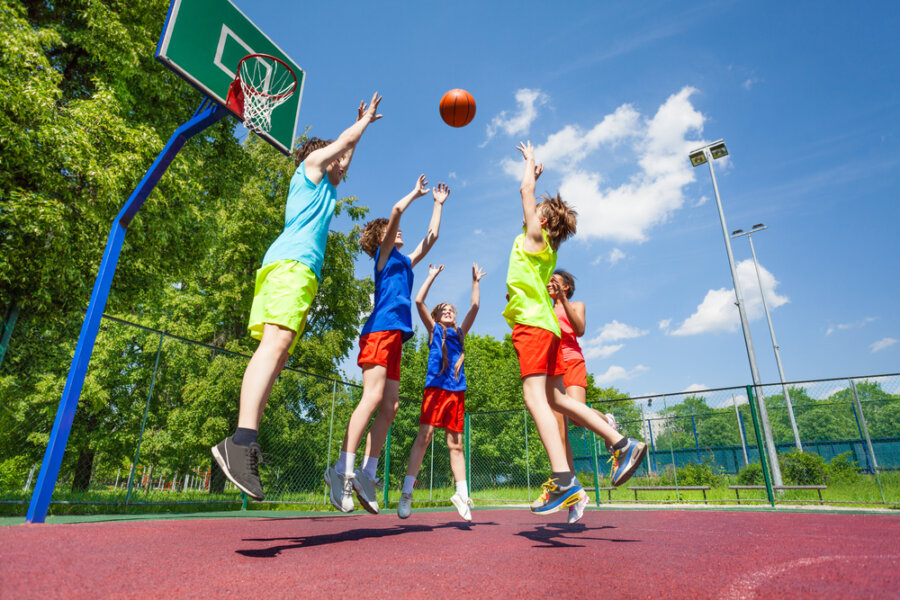 Children jump for flying ball during basketball game on the ground at sunny summer day together